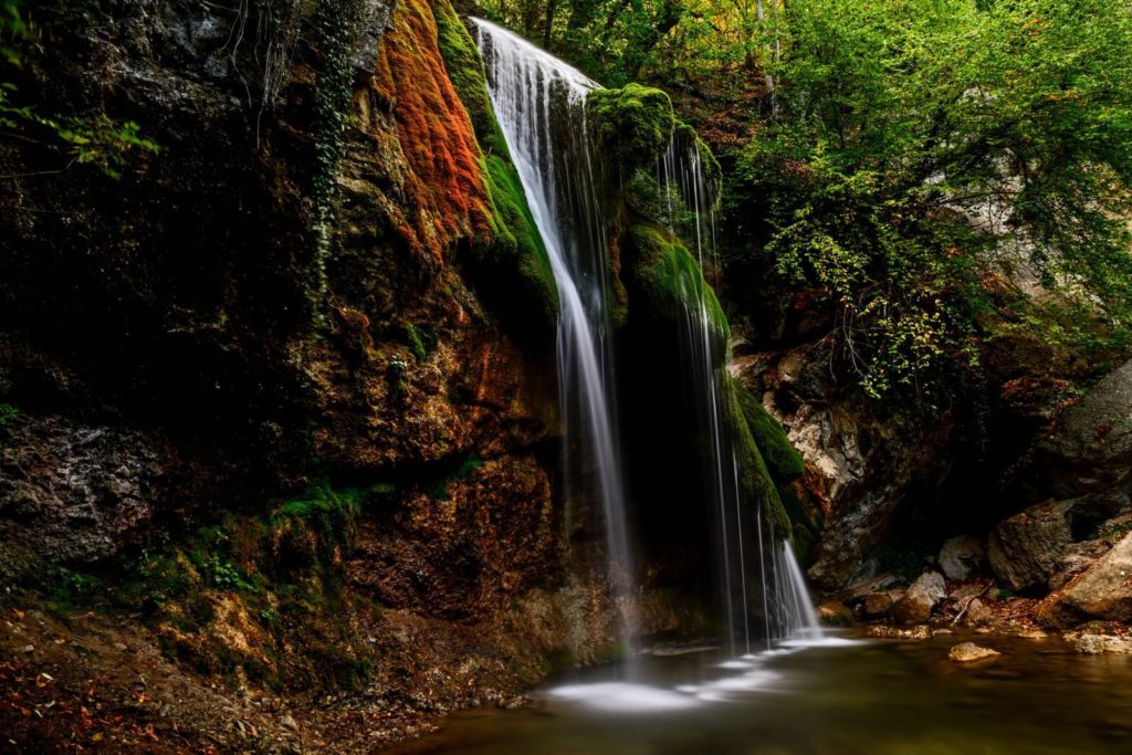 A tranquil waterfall cascading over moss-covered rocks in a lush forest setting.